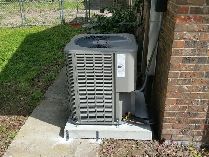Condenser on a concrete pad next to a brick wall